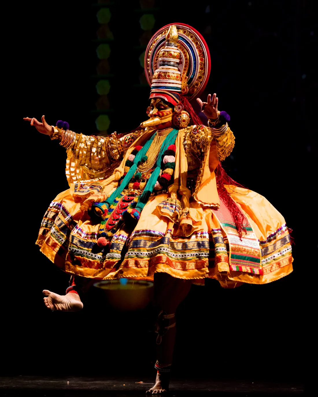 A Kathakali performer in a full ornate costume and towering headdress mid-gesture